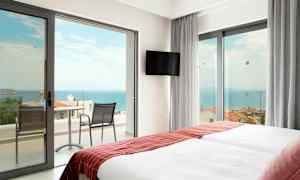 Hotellrum med två sängar och dörrar till en balkong mot havet. (AI-genererad text)