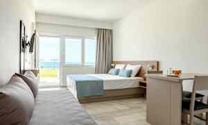 Modernt hotellrum med säng, soffa och matbord, havsutsikt utanför fönstret. (AI-genererad text)