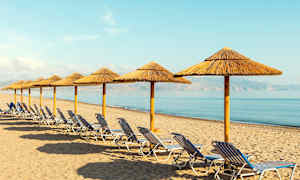 En rad med solstolar och parasoll av halm på en sandstrand vid havet. (AI-genererad text)