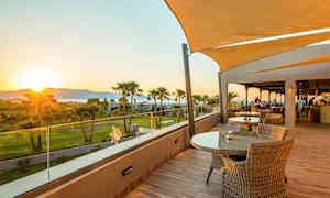 Terrass med bord och stolar samt utsikt över grönska och solnedgång. (AI-genererad text)