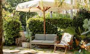 Utomhusplats med soffa, vilstol och parasoll omgiven av grönska. (AI-genererad text)