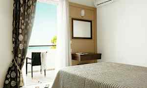 Hotellrum med säng, spegel, gardiner och balkong med utsikt mot havet. (AI-genererad text)