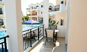 En balkong med möblemang, utsikt mot en pool och orange byggnader. (AI-genererad text)