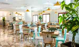 En restaurang med bord och stolar samt stora fönster och gröna växter. (AI-genererad text)