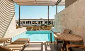 En privat terrass med solstolar, ett bord och pool, med utsikt över en byggnad på avstånd. (AI-genererad text)