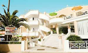 Byggnad med vit fasad och spiraltrappa, omgiven av grönska och med skylt som visar 'Rita Suites'. (AI-genererad text)