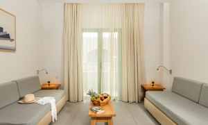 Ett vardagsrum med två grå soffor, ett bord med fruktkorg och en bok, samt gardiner framför fönstret. (AI-genererad text)