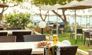 Ett bord med en tallrik sallad och ett glas öl på en terrass med utemöbler och strandparasoller i bakgrunden. (AI-genererad text)