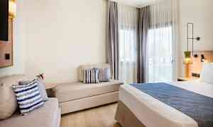 Modernt hotellrum med säng, soffa och fönster med ljusa gardiner. (AI-genererad text)