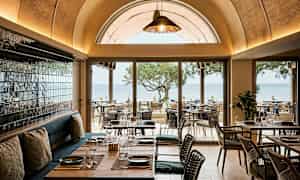 Restaurang med utsikt över havet, möbler i trä och glasdetaljer. (AI-genererad text)