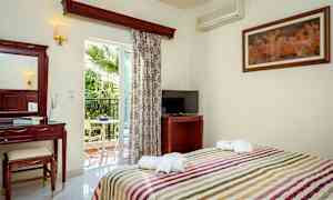 Ett hotellrum med säng, TV, spegelbord och balkong med utsikt mot en palm. (AI-genererad text)