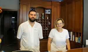 Två personer står vid en receptionsdisk med träpaneler i bakgrunden. (AI-genererad text)