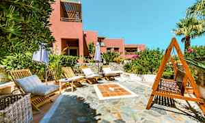 Solstolar och parasoller på en stenlagd uteplats med en rosa byggnad i bakgrunden. (AI-genererad text)