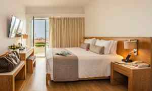 Ett hotellrum med en stor dubbelsäng, skrivbord och öppna dörrar mot en balkong med utsikt. (AI-genererad text)