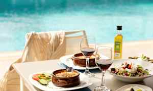 Tallrikar med grekiska rätter, två glas rött vin och en pool i bakgrunden. (AI-genererad text)