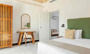 Ett sovrum med en grön sänggavel, en träskrivbord med en spegel ovanför och en trädetaljerad garderob. (AI-genererad text)