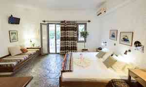 Ett hotellrum med en säng, sittbänk, bord, och en dörr som leder till en balkong. (AI-genererad text)