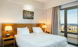 Ett rum med två enkelsängar, bordslampor och en fönsterdörr som vetter mot havet. (AI-genererad text)