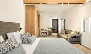 Hotellrum med en dubbelsäng i förgrunden, träinredning och ett mindre sittområde med bord och två stolar i bakgrunden. (AI-genererad text)