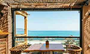 En uteplats med bord och stolar, utsikt över havet och stranden genom en ram. (AI-genererad text)