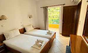 Ett hotellrum med två enkelsängar och handdukar placerade ovanpå. Rummet har en balkong med utsikt över grönska. (AI-genererad text)