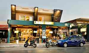 Fasad av Akatos Hotel med bilar och motorcyklar parkerade framför. (AI-genererad text)