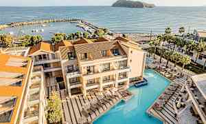 Bild av hotellområde med pool och solstolar intill havet. I bakgrunden syns en liten marina och en ö. (AI-genererad text)