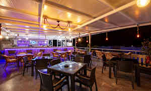 En utomhusbar med stolar och bord, upplyst med varm belysning vid nattid. (AI-genererad text)