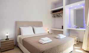 Ett hotellrum med en dubbelsäng utrustad med beige sängöverkast och två uppsättningar handdukar, samt sidobord och garderob. (AI-genererad text)