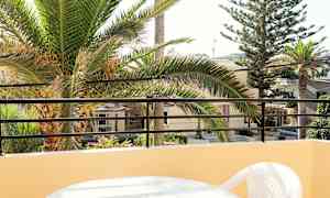 Vy från balkong med ett bord och plaststol, palmträd och byggnader i bakgrunden. (AI-genererad text)