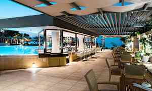 Restaurang som vetter mot en pool och utomhusområde med havsutsikt på kvällen. (AI-genererad text)