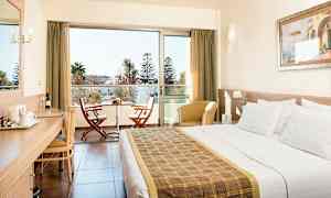 Hotellrum med en dubbelsäng, skrivbord, sittmöbler och en balkong med två stolar och ett bord. (AI-genererad text)