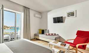 Ett hotellrum med sittgrupp, säng och utsikt mot en strand genom en glasdörr. (AI-genererad text)