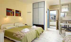 Två bäddar med grön sängklädsel och blommönstrade överkast i ett rum med skåp, köksbord och dörr till balkong. (AI-genererad text)