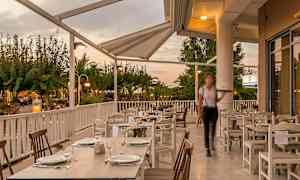 Uteservering med dukade bord under tak, omgiven av grönska. (AI-genererad text)