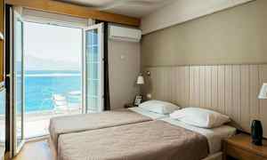 Ett hotellrum med två enkelsängar och en öppen balkongdörr som vetter mot havet. (AI-genererad text)