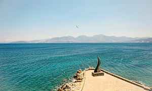 En stenig strand och hav med ett konstverk synligt på en brygga. (AI-genererad text)