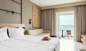 Hotellrum med säng, soffa och balkong med havsutsikt. (AI-genererad text)