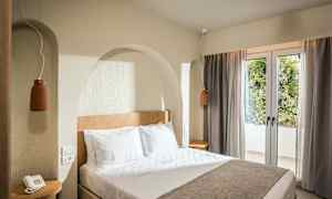 Ett hotellrum med en dubbelsäng, sängbord och fönster med draperier. (AI-genererad text)