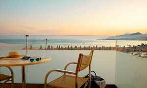 Utsikt från en terrass mot havet med solnedgång och strandparasoller i bakgrunden. (AI-genererad text)