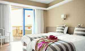 Ett hotellrum med två enkelsängar, randiga sängkläder och en dörr till en balkong. (AI-genererad text)