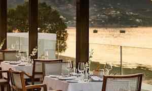 En uteservering med dukade bord vid strandkanten och en utsikt över havet. (AI-genererad text)