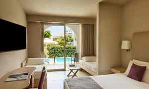 Ett hotellrum med en dubbelsäng, en skrivhörna, och en extra säng. Utanför syns en terrass och en pool. (AI-genererad text)