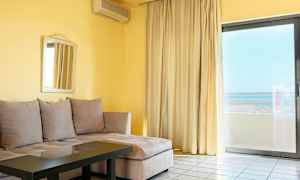 Ett vardagsrum med beige hörnsoffa, glasbord, spegel på väggen och stor fönsterdörr mot både gardiner och utsikt. (AI-genererad text)