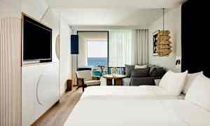 Ett hotellrum med två bäddar, sittmöbler och en balkong med utsikt över havet. (AI-genererad text)