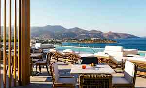 En terrass med utsikt över havet och berg i bakgrunden, med solstolar och bord. (AI-genererad text)