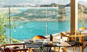 En restaurang med ett bord dukat för frukost, med utsikt över havet och omgivande landskap. (AI-genererad text)