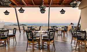 En restaurang med bord och stolar på en terrass med utsikt över havet. (AI-genererad text)