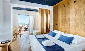 Ljust hotellrum med dubbelsäng och trädetaljer, utsikt mot balkong och hav. (AI-genererad text)