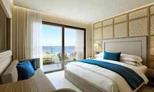 Ett hotellrum med en dubbelsäng, soffa, och utsikt mot havet från en balkong. (AI-genererad text)